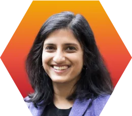 A woman with long dark hair and a purple blazer smiles in front of a hexagonal orange and red gradient background.