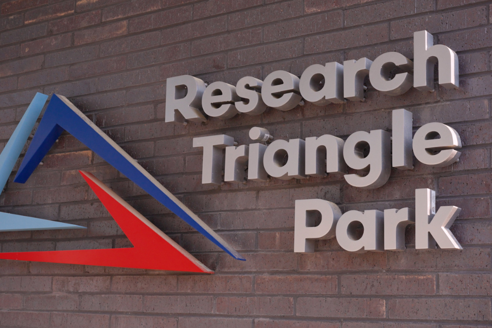 Metallic letters spelling "Research Triangle Park" are mounted on a brick wall next to a geometric logo with blue and red triangles.