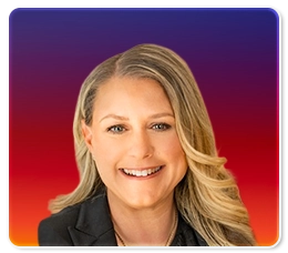 Smiling woman with long blonde hair, wearing a black blazer, in front of a gradient background transitioning from purple at the top to red and orange at the bottom.