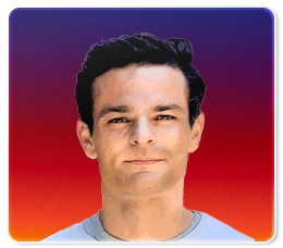 A man with short dark hair and fair skin is facing forward, wearing a light-colored shirt. The background is a gradient of purple, red, and orange.