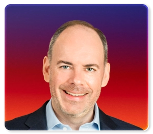 A smiling man with short hair and a trimmed beard, wearing a dark jacket and white shirt, is pictured in front of a gradient background that transitions from purple at the top to red and orange at the bottom.